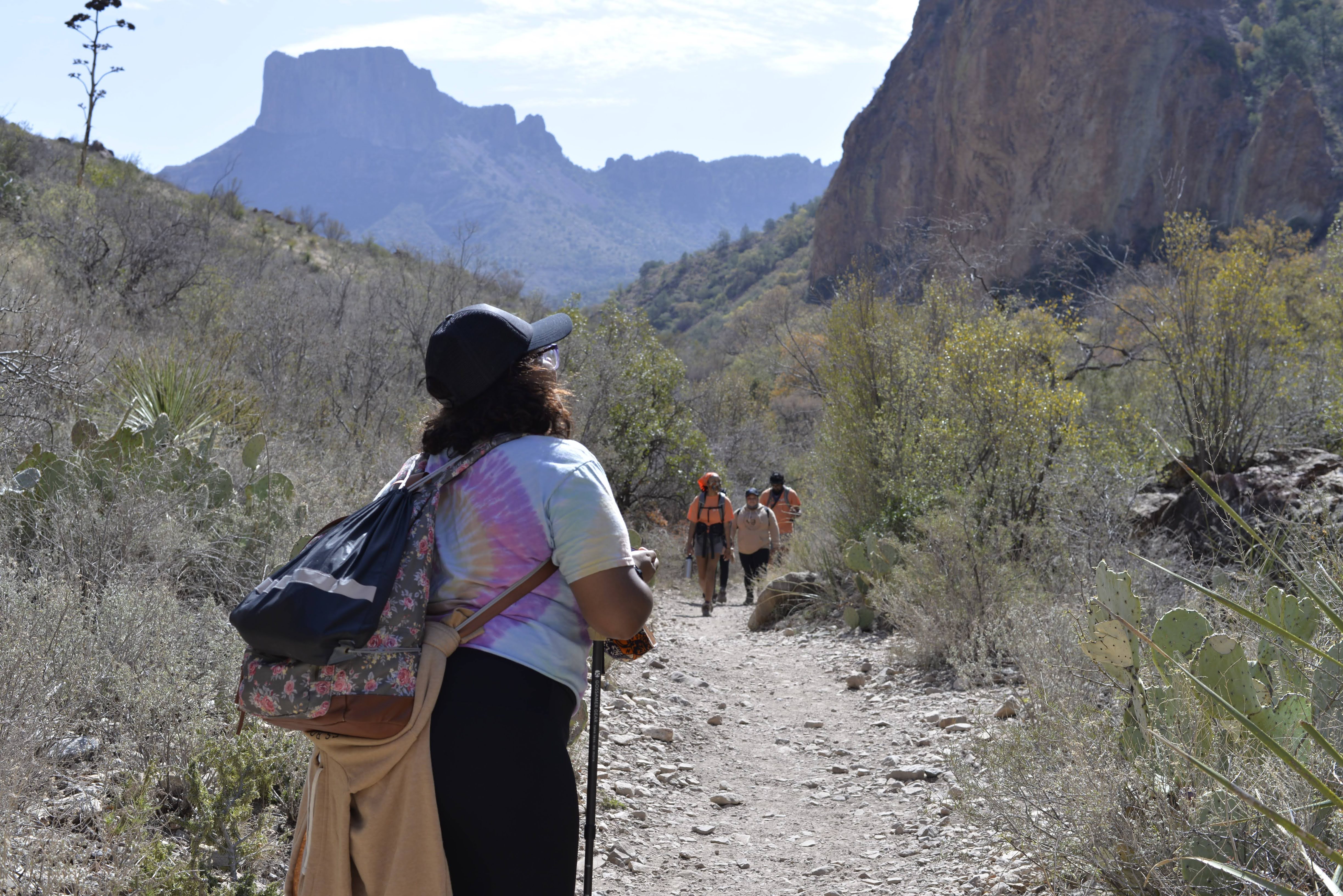 A young person stands looking down a trail with their back to the camera